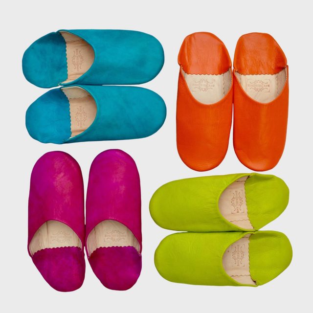 Four pairs of colorful slippers arranged symmetrically on a plain background. Slippers are turquoise, orange, magenta, and lime green.