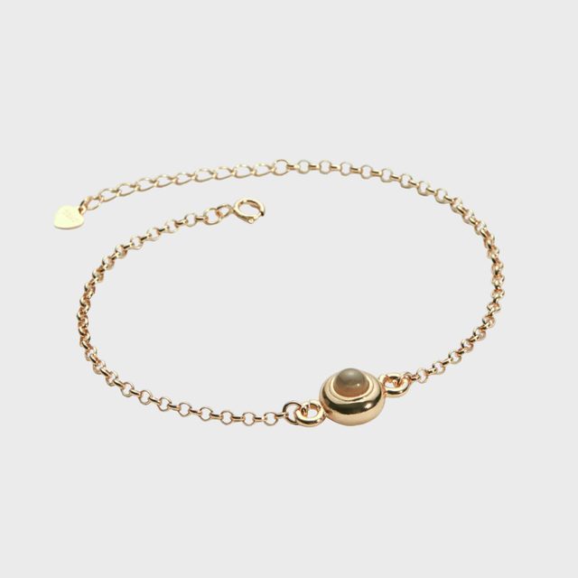 Gold chain bracelet displaying a central pearl accent, lying flat against a plain white background.