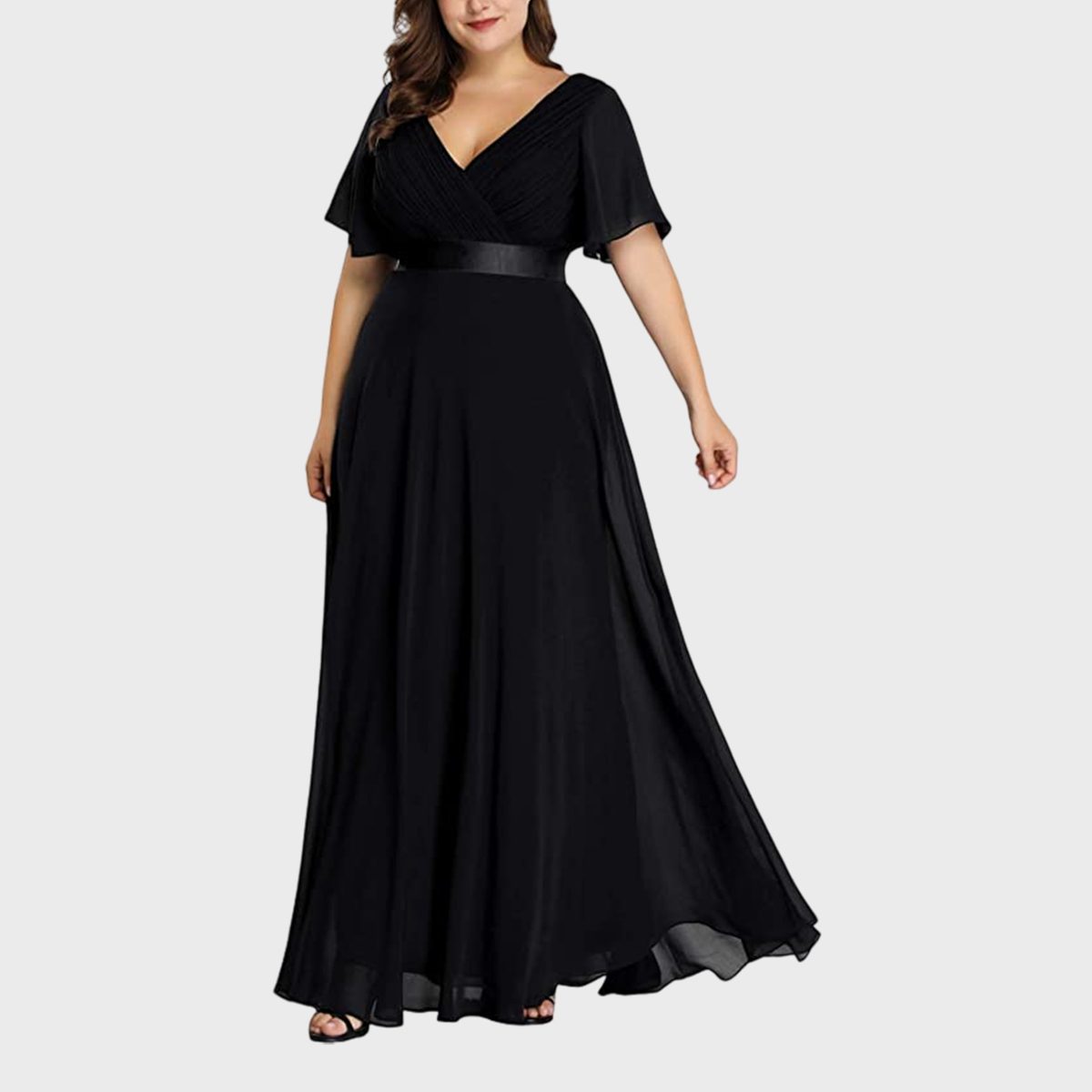 A woman wears a long, flowing black dress with short sleeves, standing against a plain, light background.