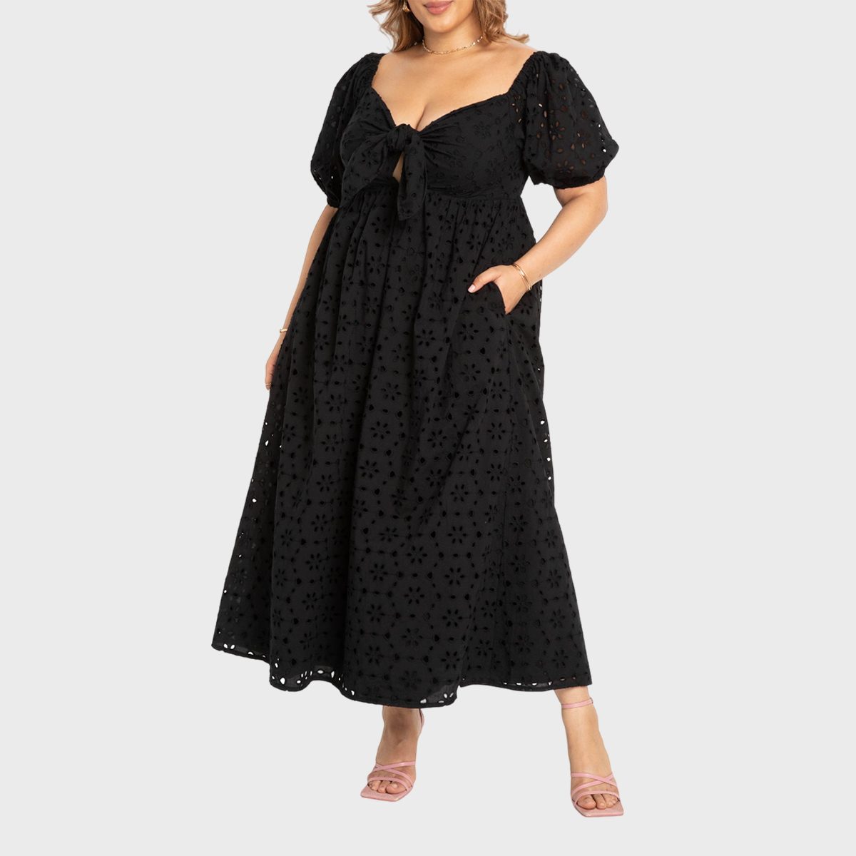 A person wears a black, floral-patterned maxi dress with puffed sleeves, standing against a plain, light gray background.