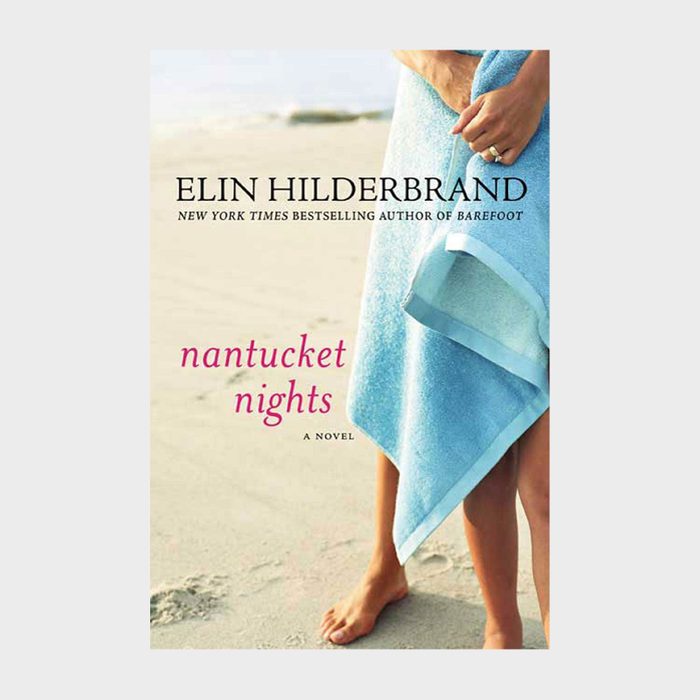 Feet stand on sand holding a blue towel. 