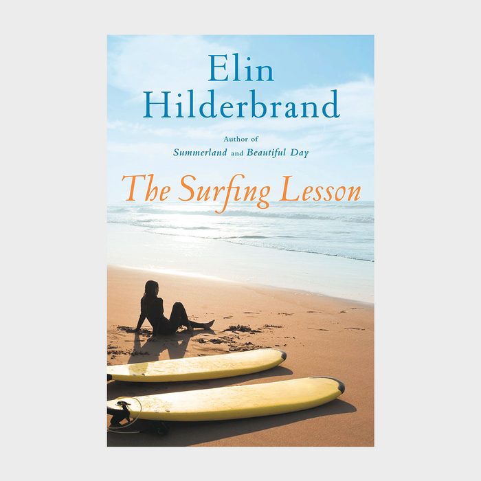 Two surfboards rest on sandy beach; person sits, ocean waves under clear sky. Text: 