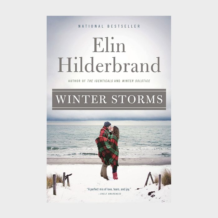Couple embraces wrapped in plaid blanket, facing ocean; snowy beach surroundings. Book title 