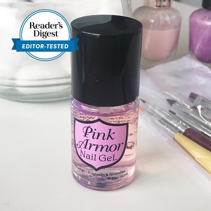 Pink Armor Nail Gel bottle stands on a tabletop, surrounded by nail care tools and polish bottles. 