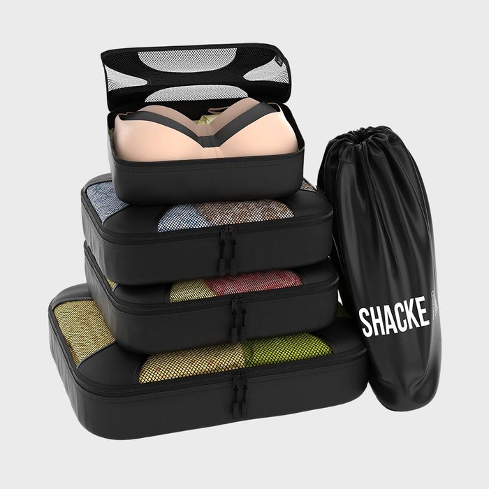 Packing cubes stack neatly with clothes inside, alongside a drawstring bag labeled 