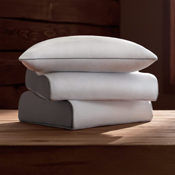 Three white pillows are stacked neatly on a wooden table, set against a dark brown wooden background.