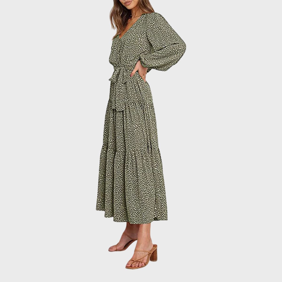 A woman models a long, green patterned dress with puffy sleeves, standing sideways in a neutral studio setting, wearing tan heels.