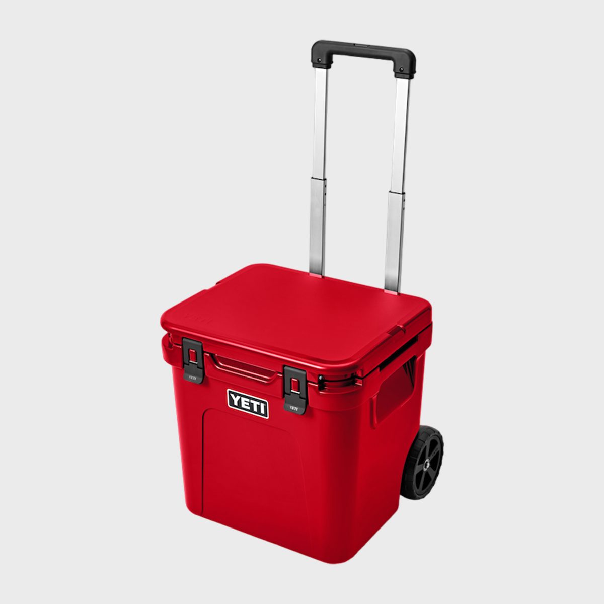 Red wheeled cooler with extended handle, displaying "YETI" logo, situated against a plain background.