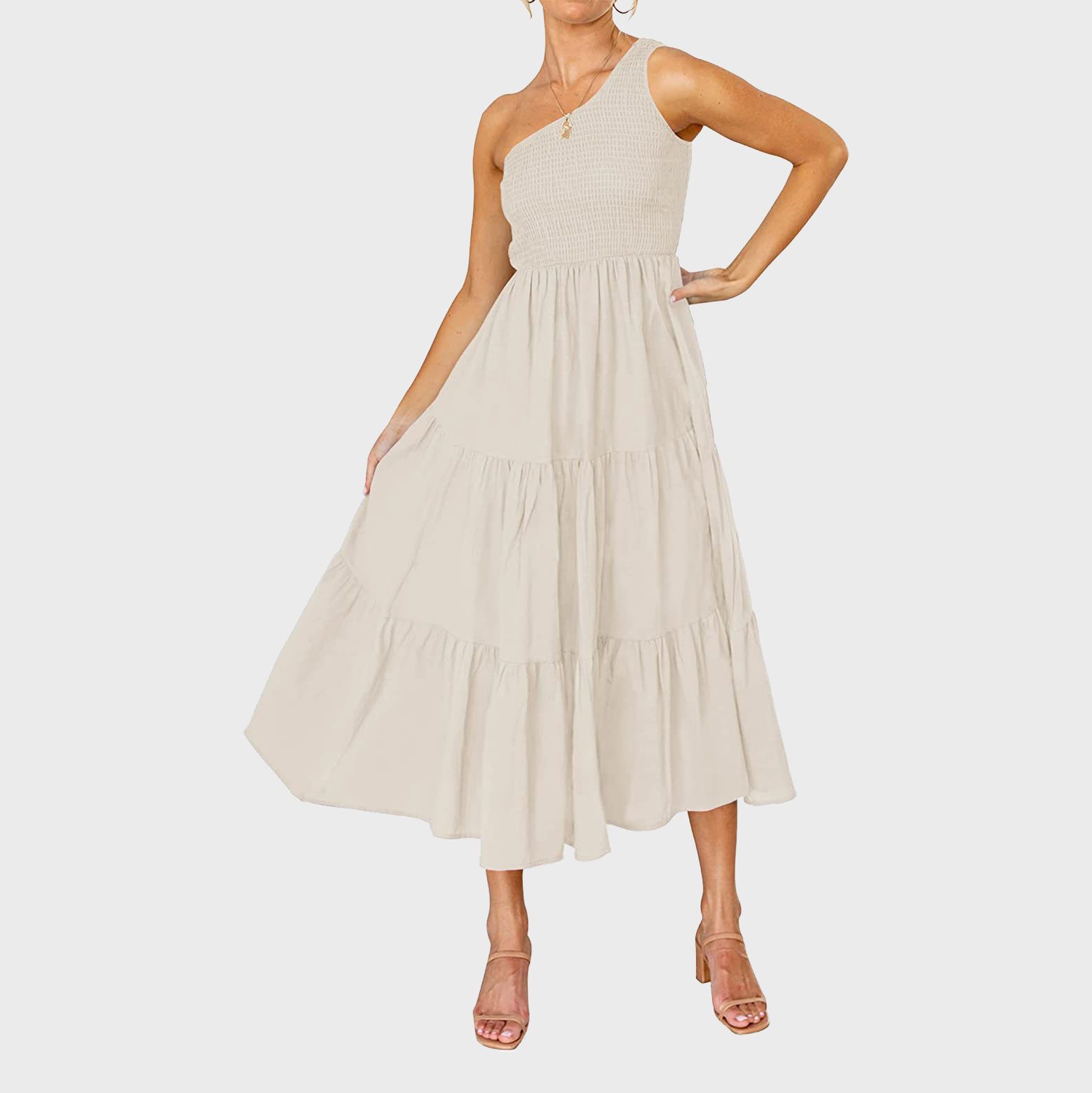 A woman wears a one-shoulder cream dress, standing confidently with hands on hips, against a plain background.
