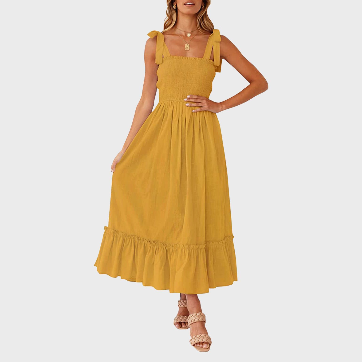 Yellow sundress is worn by a woman standing on a plain white background, her right hand resting on her hip.