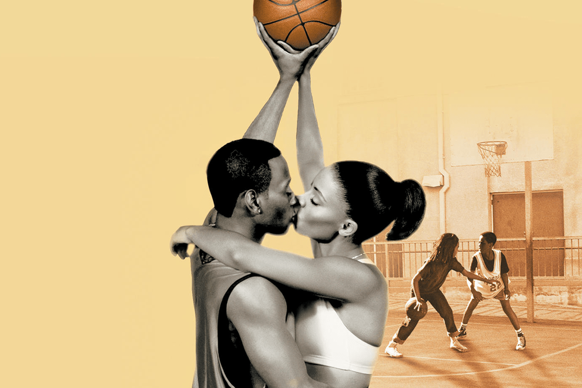 A couple kisses, holding a basketball above them, on a court where two children play in the background.