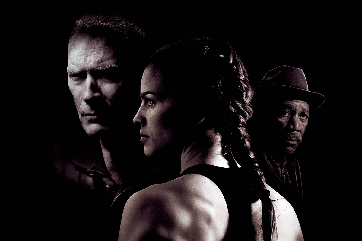 Three people, staring intently; man on the left, woman in foreground with braided hair, man on the right wearing a hat; dark background.