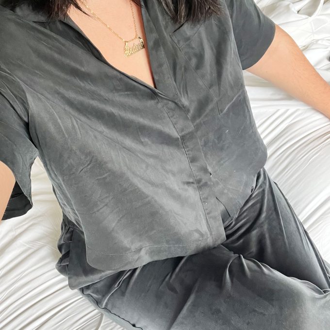 Person lounging on bed, wearing dark silky pajamas, necklace says 
