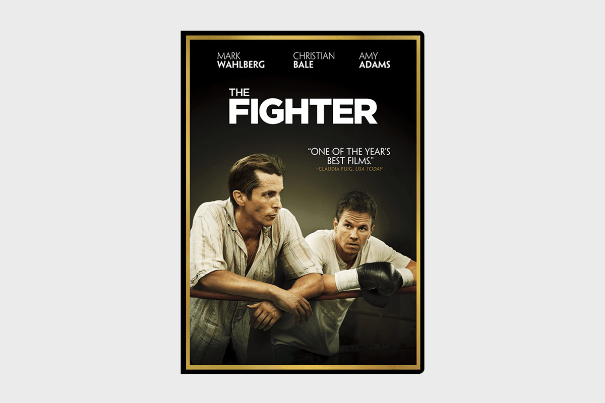Two men rest on boxing ropes; one wears gloves, both appear serious. The text above reads "THE FIGHTER" with a favorable review quote.