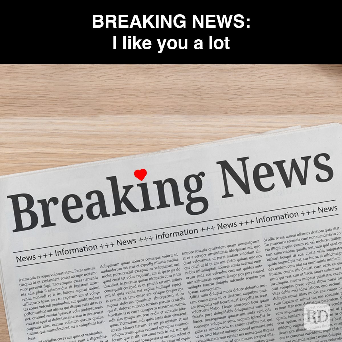 Newspaper headline states "Breaking News" with a small red heart above "i". Caption reads: "BREAKING NEWS: I like you a lot." Background is a wood surface.
