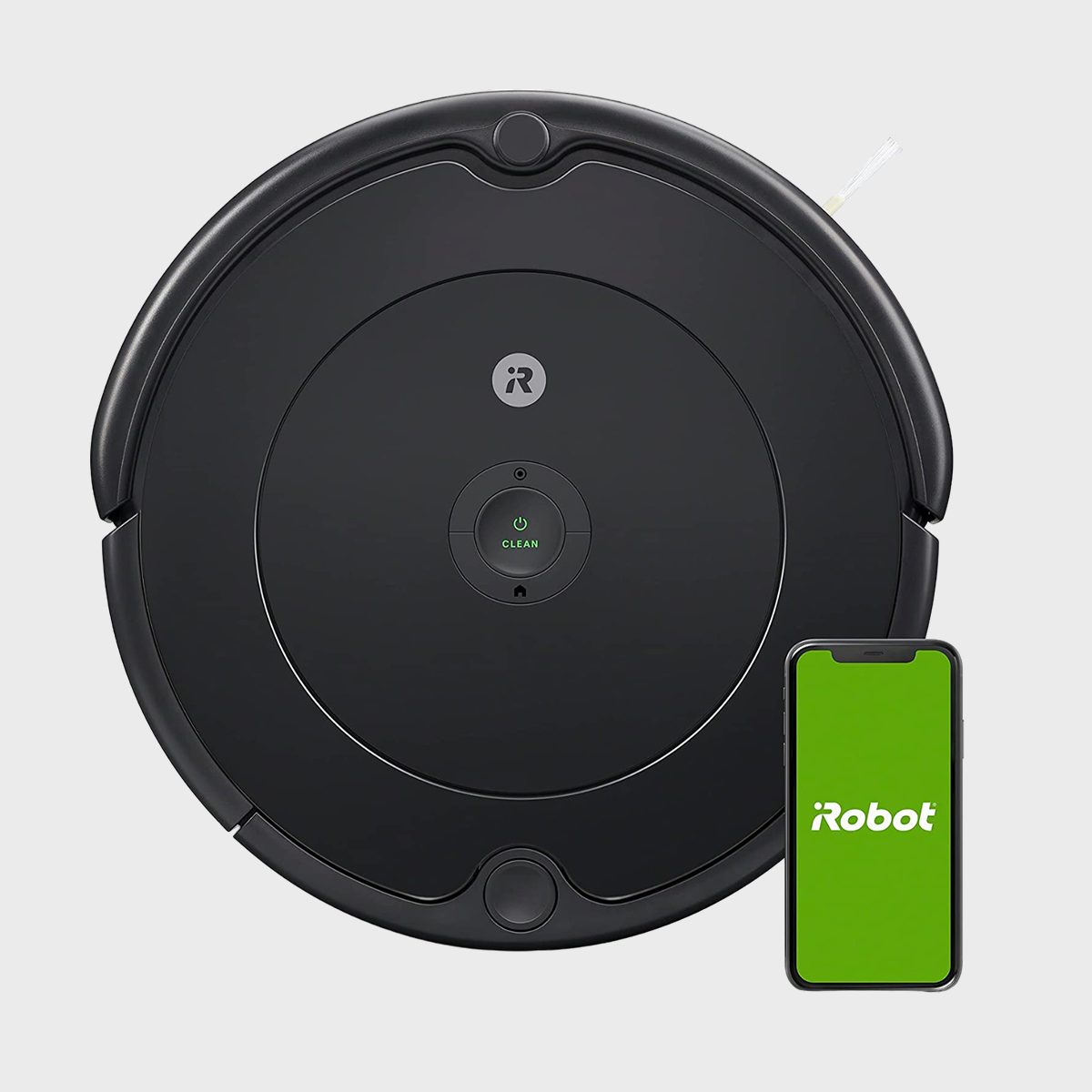 Robot vacuum sits idle with app displaying "iRobot" on phone screen; set against a plain, light gray background.