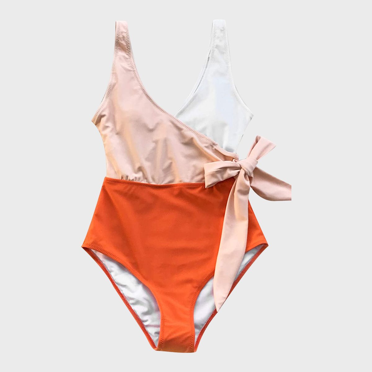 A colorful swimsuit lies flat, featuring an asymmetric design with peach and white top, orange bottom, and a side bow tie on a plain background.