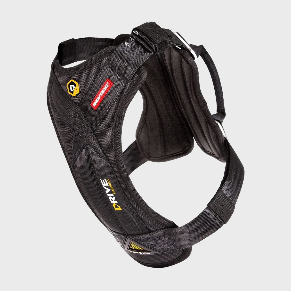 A black safety harness is suspended, displaying branding labels, with padded straps and metal buckles in a studio setting.