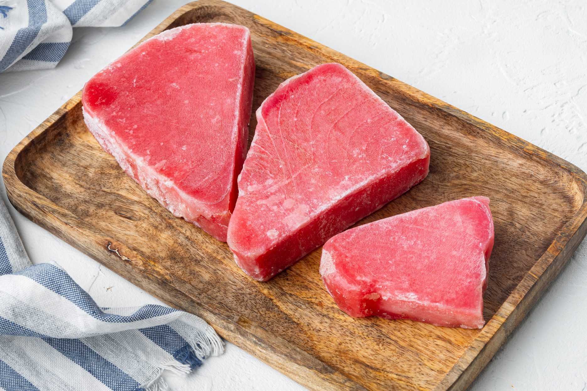 Raw frozen tuna fish fillet, on wooden tray, on white stone background