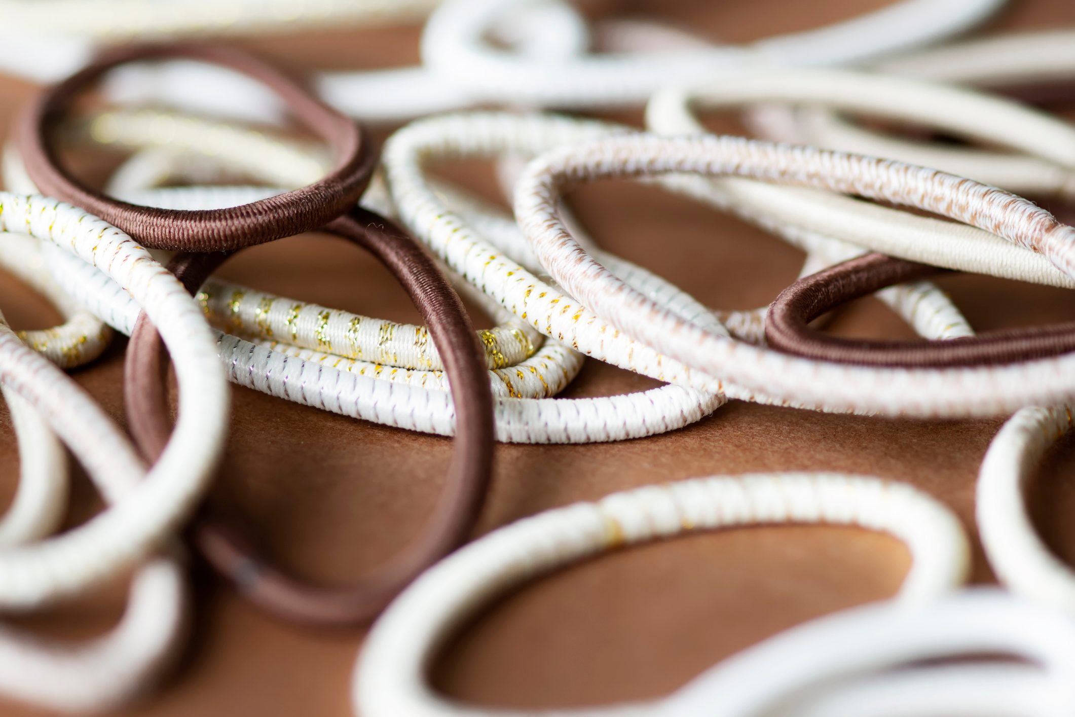 Elastic hair bands lie scattered on a brown surface, featuring various colors and patterns, including white, brown, and gold accents.