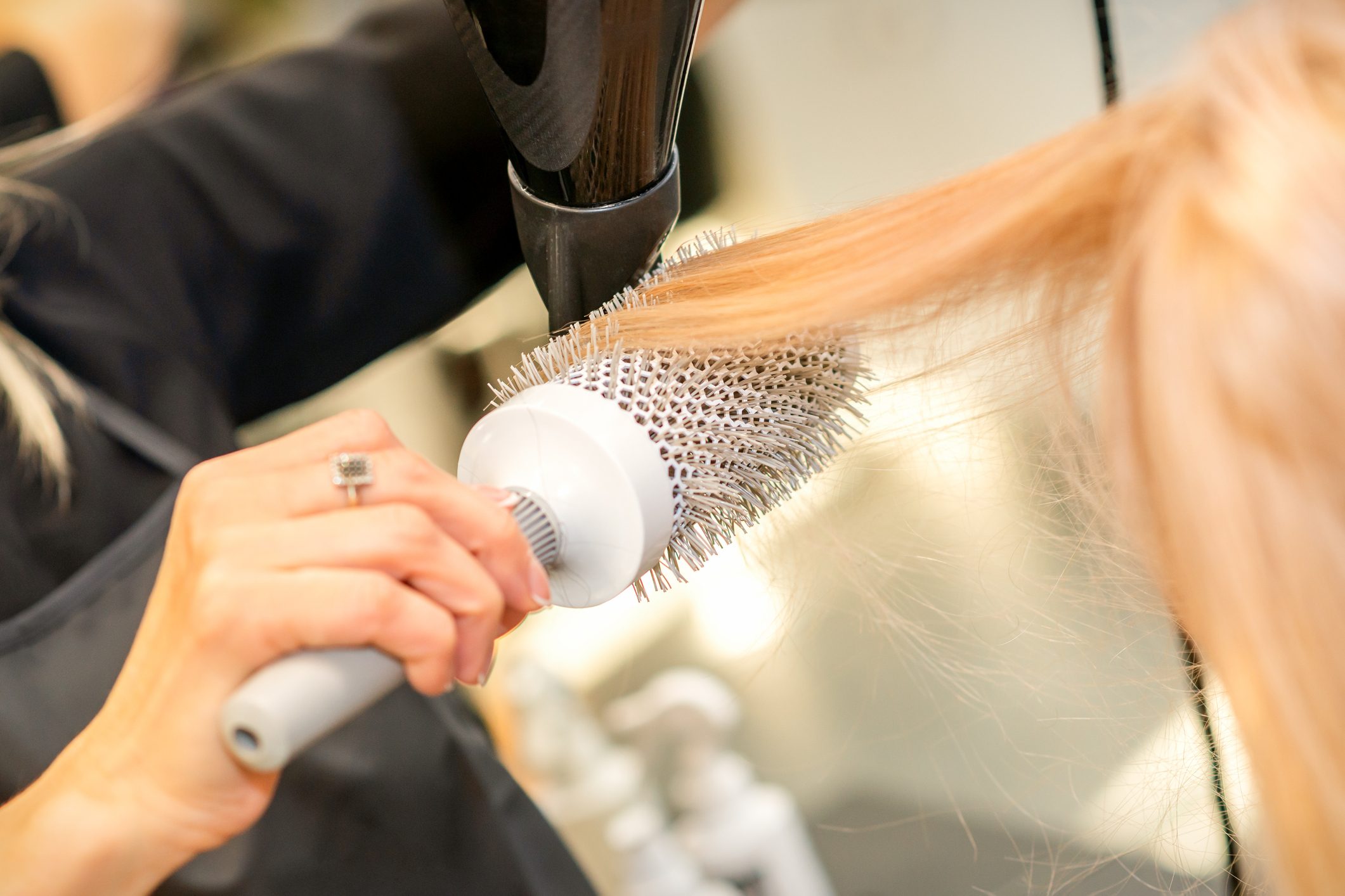 Hairbrush styling blonde hair while blow-drying in a salon setting.