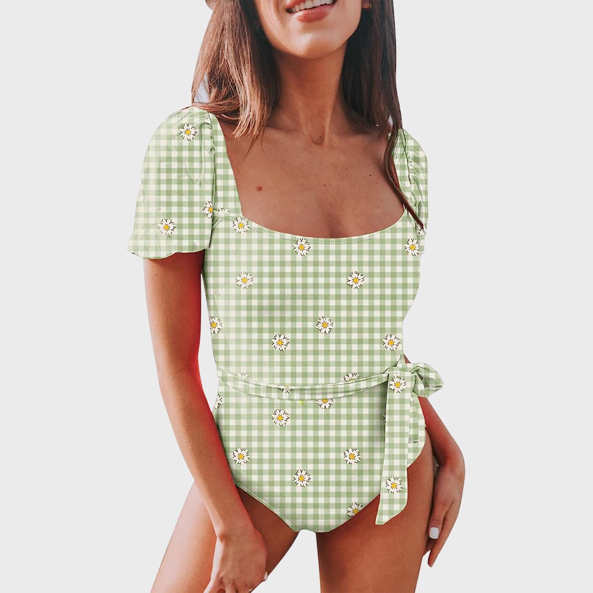 Woman wearing a green gingham swimsuit with daisy print, smiling against a plain white background.