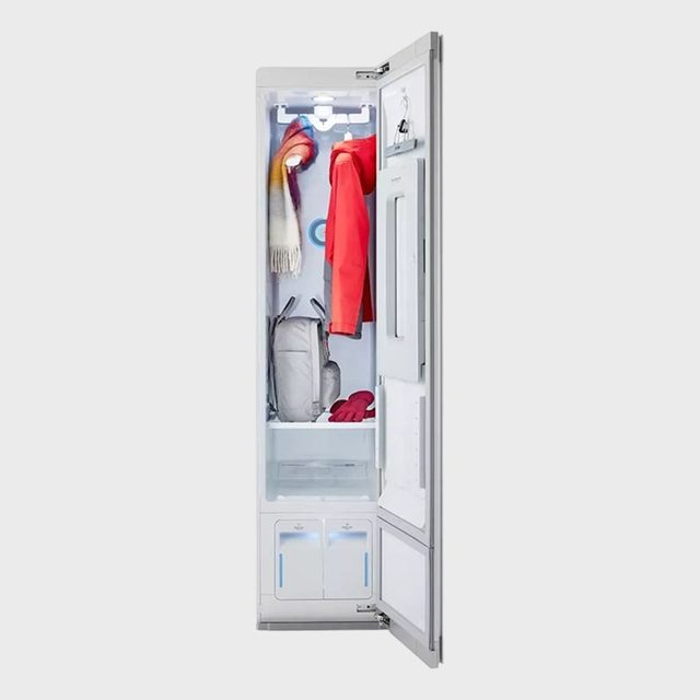 Wardrobe steams garments inside a narrow white cabinet, containing a red coat, multicolored scarf, and gloves, emphasizing clothing care technology in a home setting.