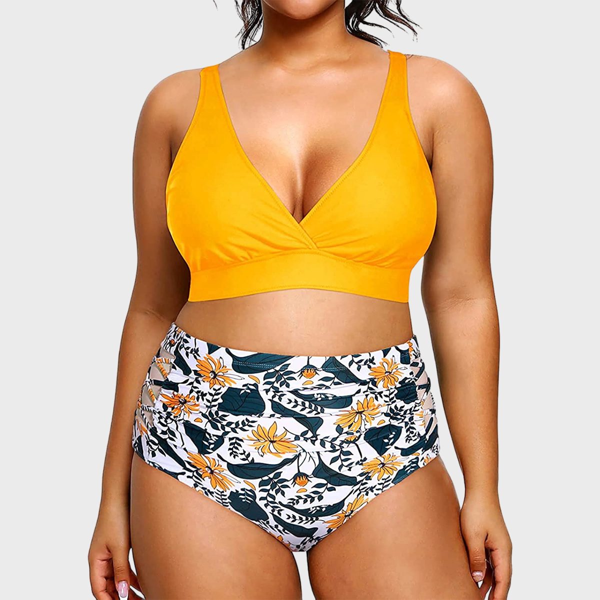 Woman wears bright yellow bikini top, floral high-waisted bottoms; standing against plain, neutral background.