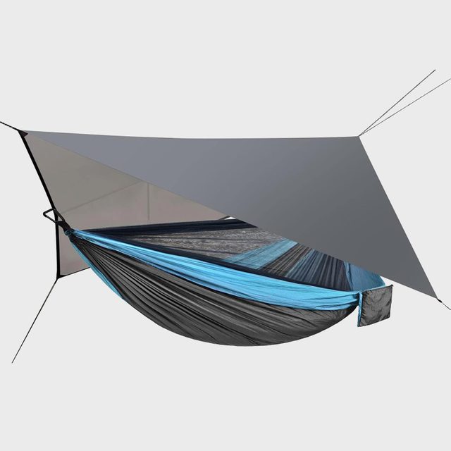 Hammock suspended, covered with a gray tarp, set against a plain light background; shows outdoor gear.