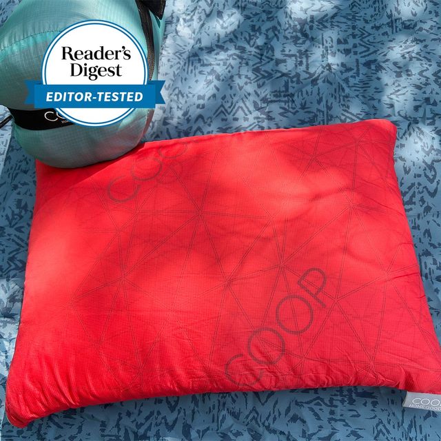 Red pillow lies on a patterned surface with a blue sleeping bag. Seen alongside is a 