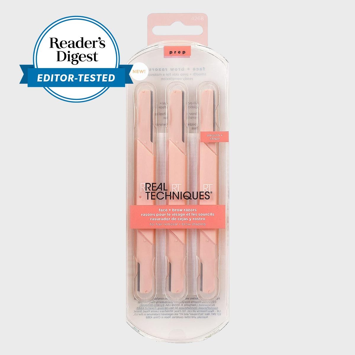 Pink face and brow razors are packaged in clear plastic, featuring "Real Techniques" branding; a Readerâ€™s Digest â€œEditor-Testedâ€ badge is displayed nearby.