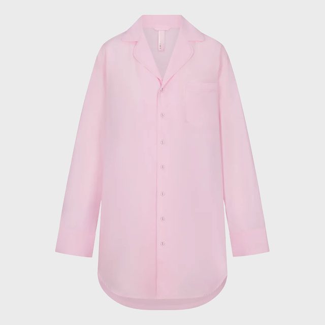 A pink button-up shirt hangs against a plain white background, featuring a pointed collar and a chest pocket.