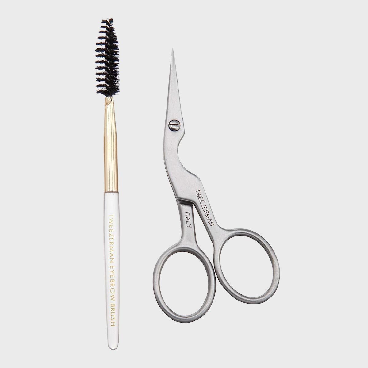 Eyebrow brush and scissors lying side-by-side on a plain background. Text reads: "TWEEZERMAN EYEBROW BRUSH" and "TWEEZERMAN ITALY."