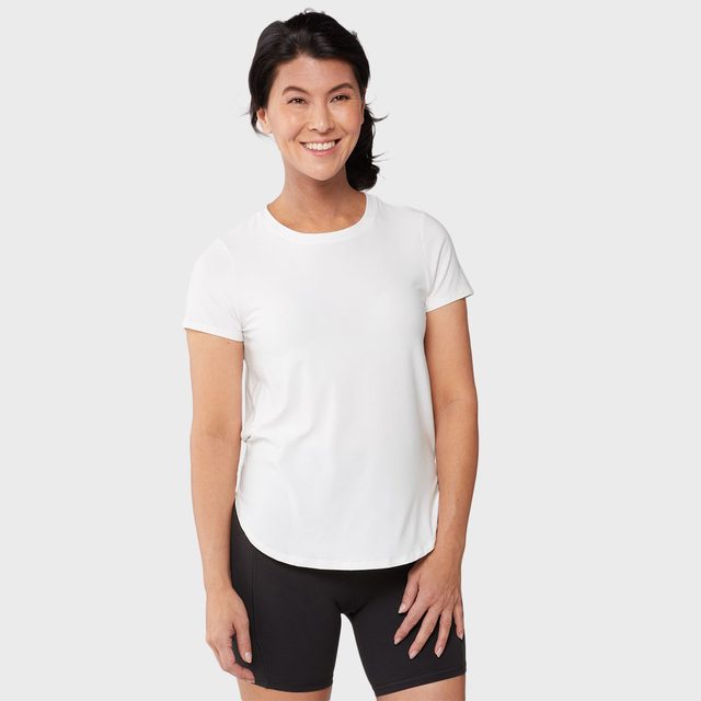 A person smiles, standing casually, wearing a white T-shirt and black shorts against a plain light background.