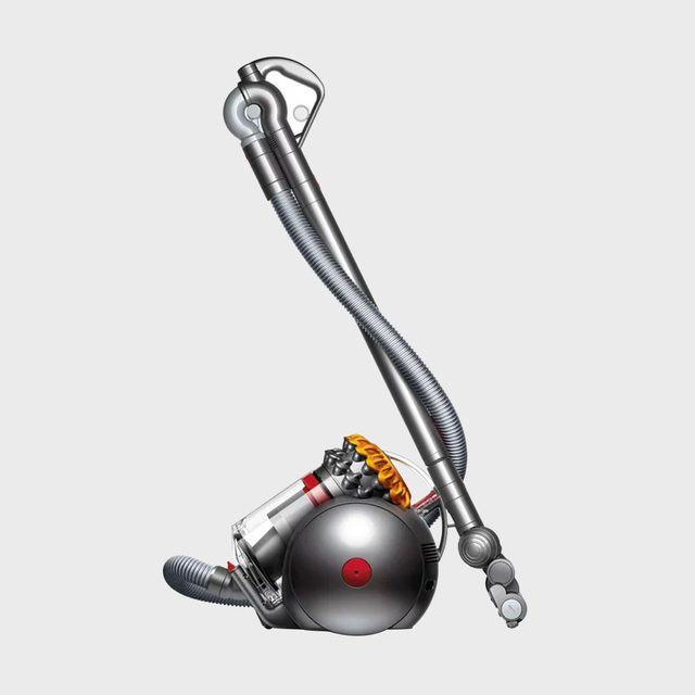 A futuristic vacuum cleaner stands idle, silver in color, with sleek, curved design and a cylindrical body against a plain gray background.