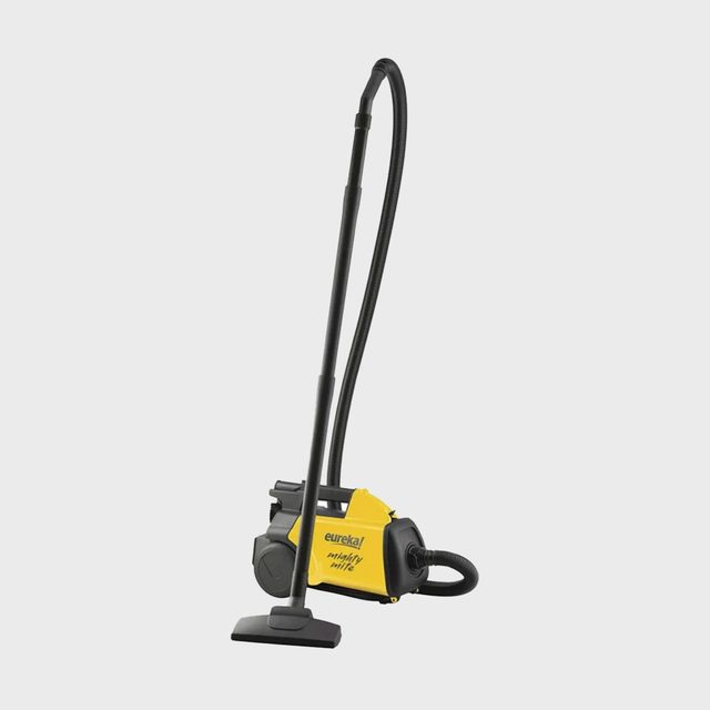 Vacuum cleaner standing on floor, connected with hose and nozzle, against plain background. Text reads 