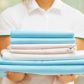Folded towels rest on person's arms, against a blurred background, suggesting an indoor setting, with a focus on neatness and cleanliness.