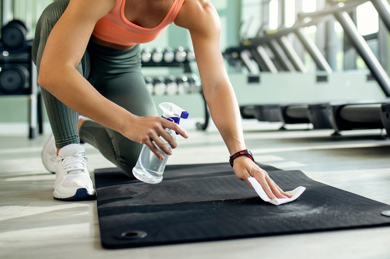 Happy athletic woman disinfecting exercise man before working out in a gym.