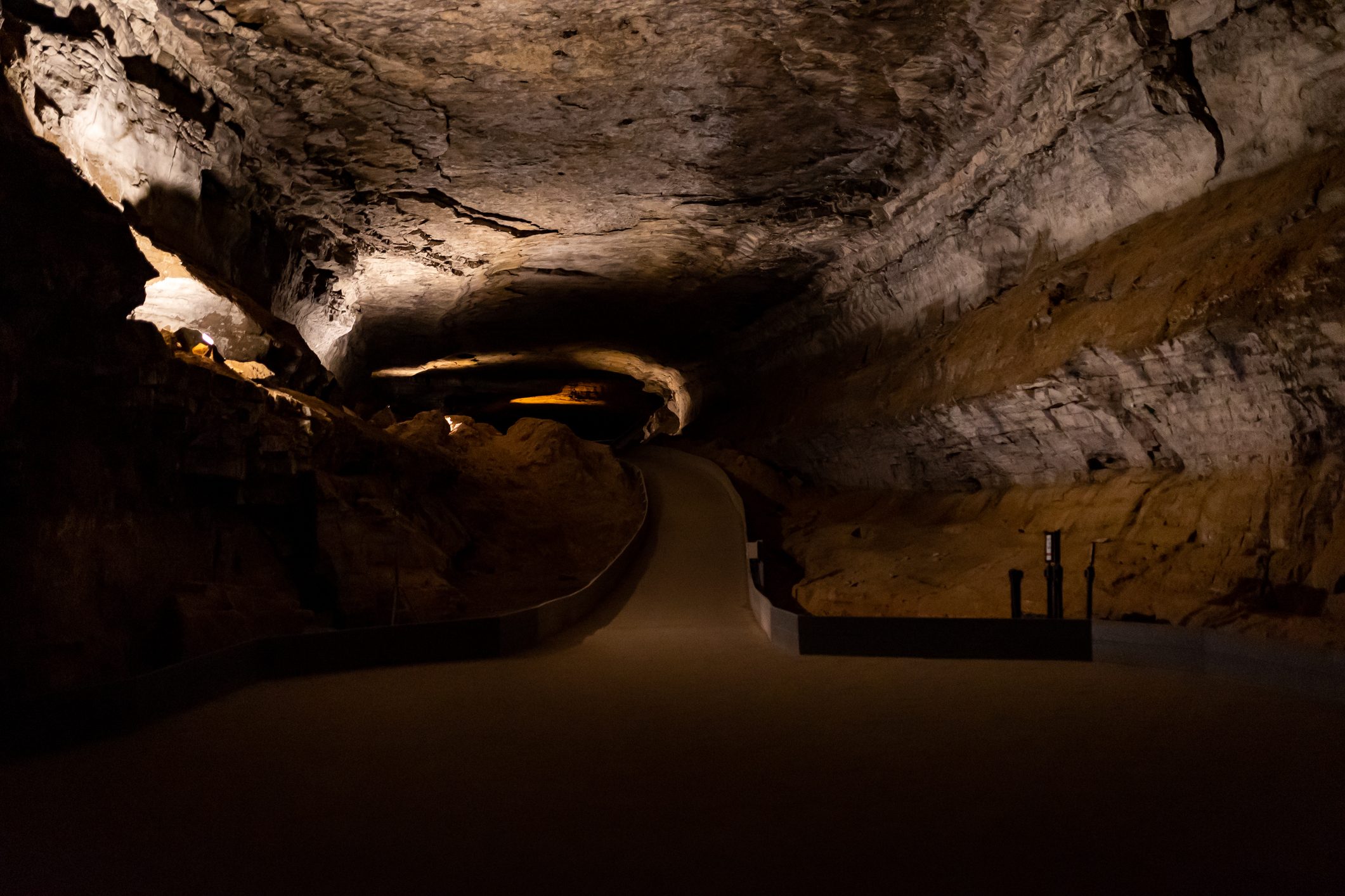 A dimly lit cave tunnel curves gently, surrounded by textured rock walls, creating a mysterious underground passage.