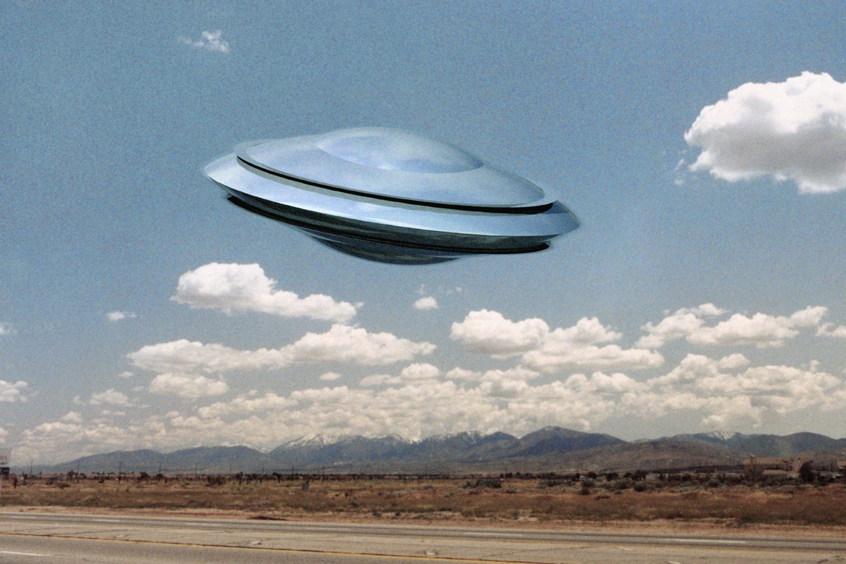 A metallic saucer hovers above a desert landscape with mountains and scattered clouds in the background.