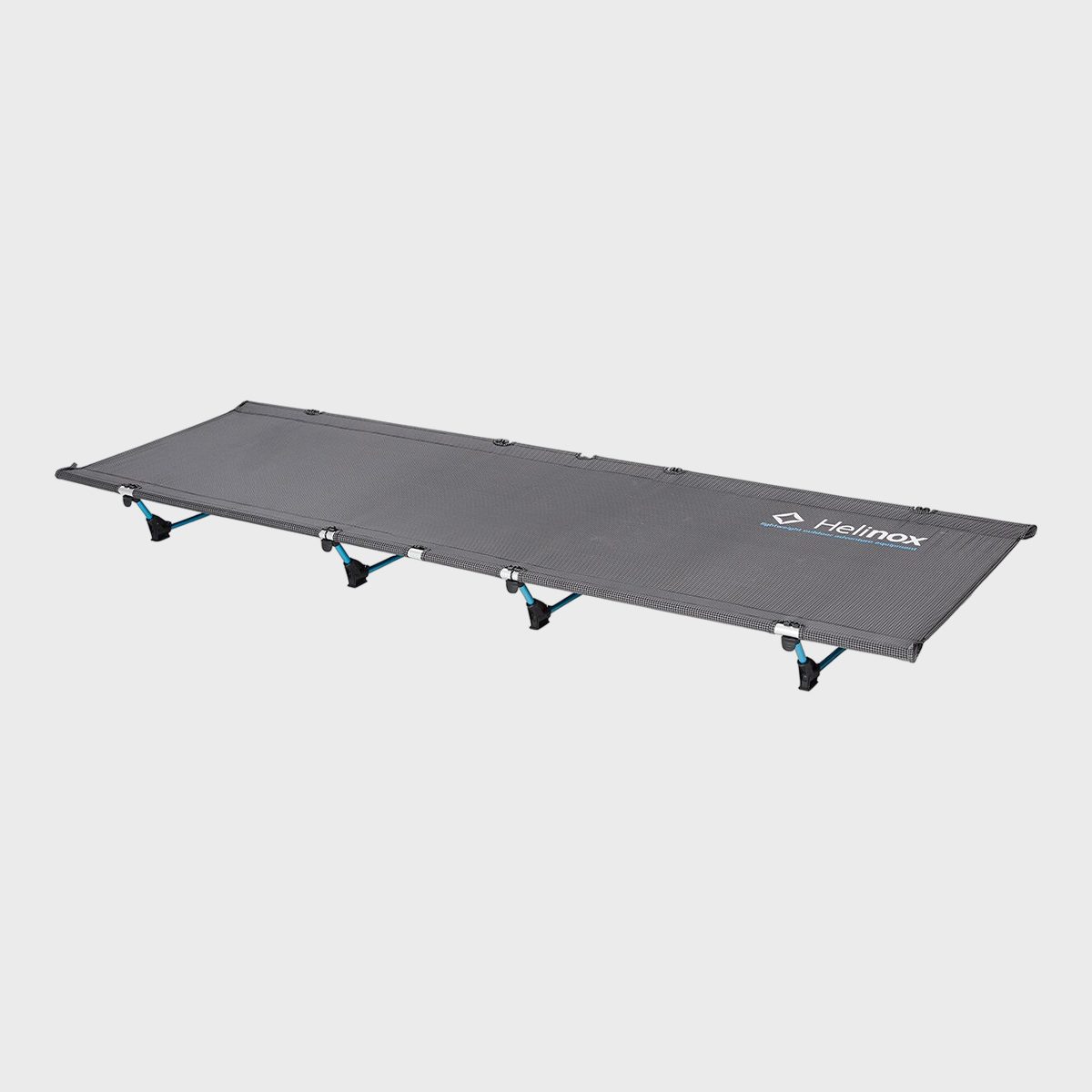 A lightweight, gray camping cot with stabilizing legs rests against a plain white background. Text reads "Helinox" on its surface.