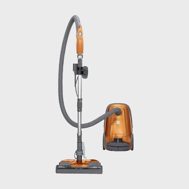 Orange canister vacuum cleaner stands upright with hose extended, set against a plain white background.