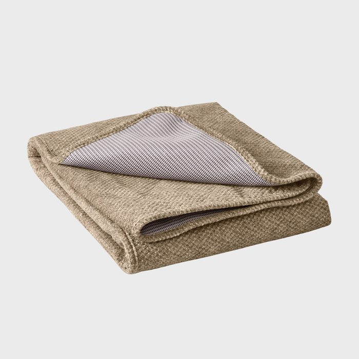 A beige blanket with a folded corner reveals a striped underside, resting on a plain white surface.