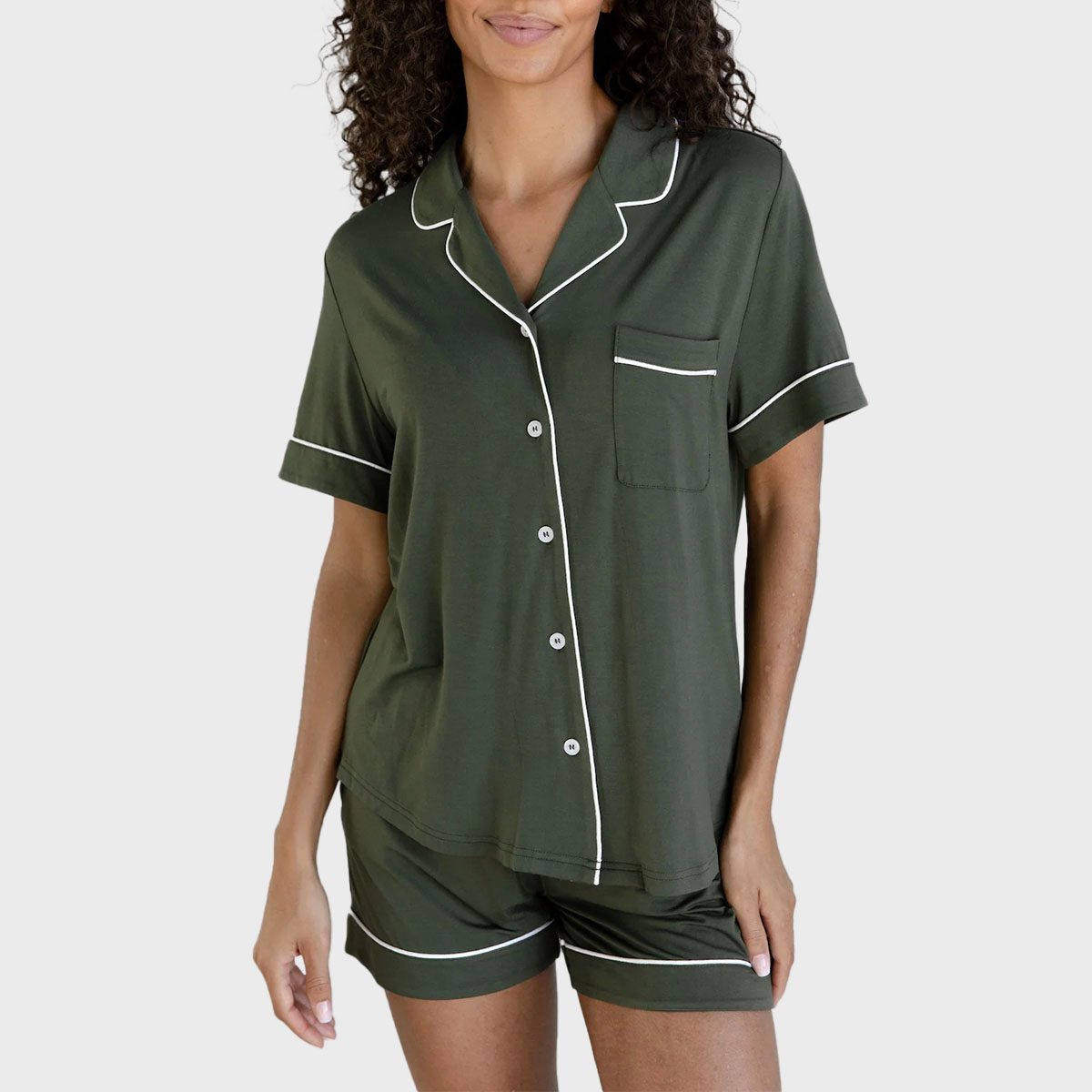 Person wearing a dark green button-up pajama set with white piping, standing against a plain, light background.