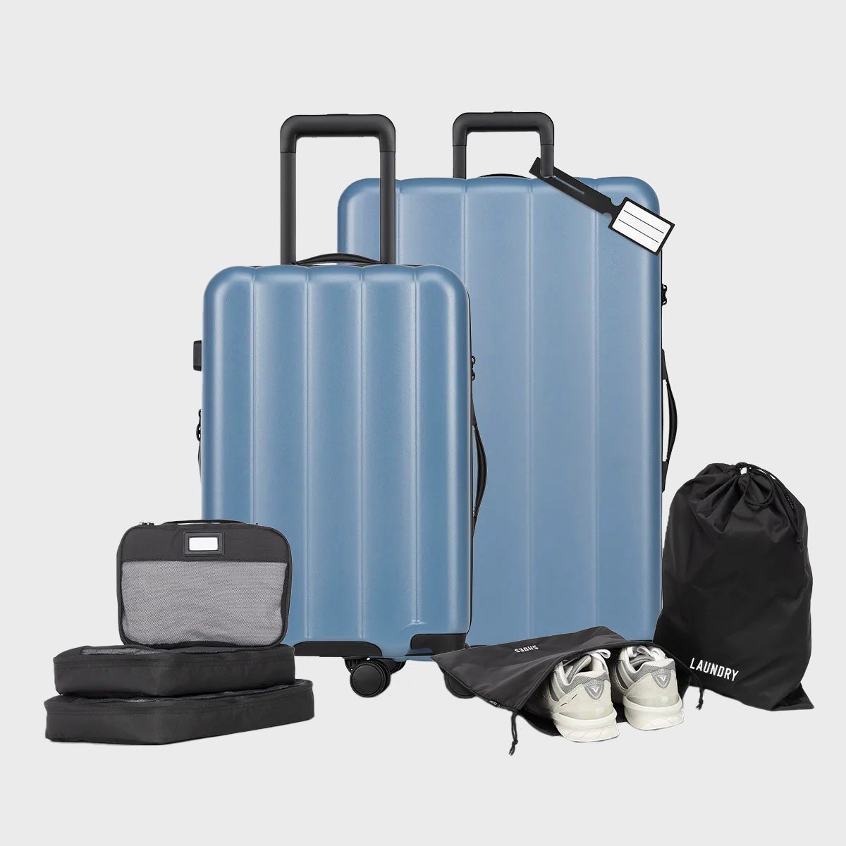 Suitcases standing upright on a surface, accompanied by packing cubes, shoe bags, and a laundry bag, in a minimalist setting.