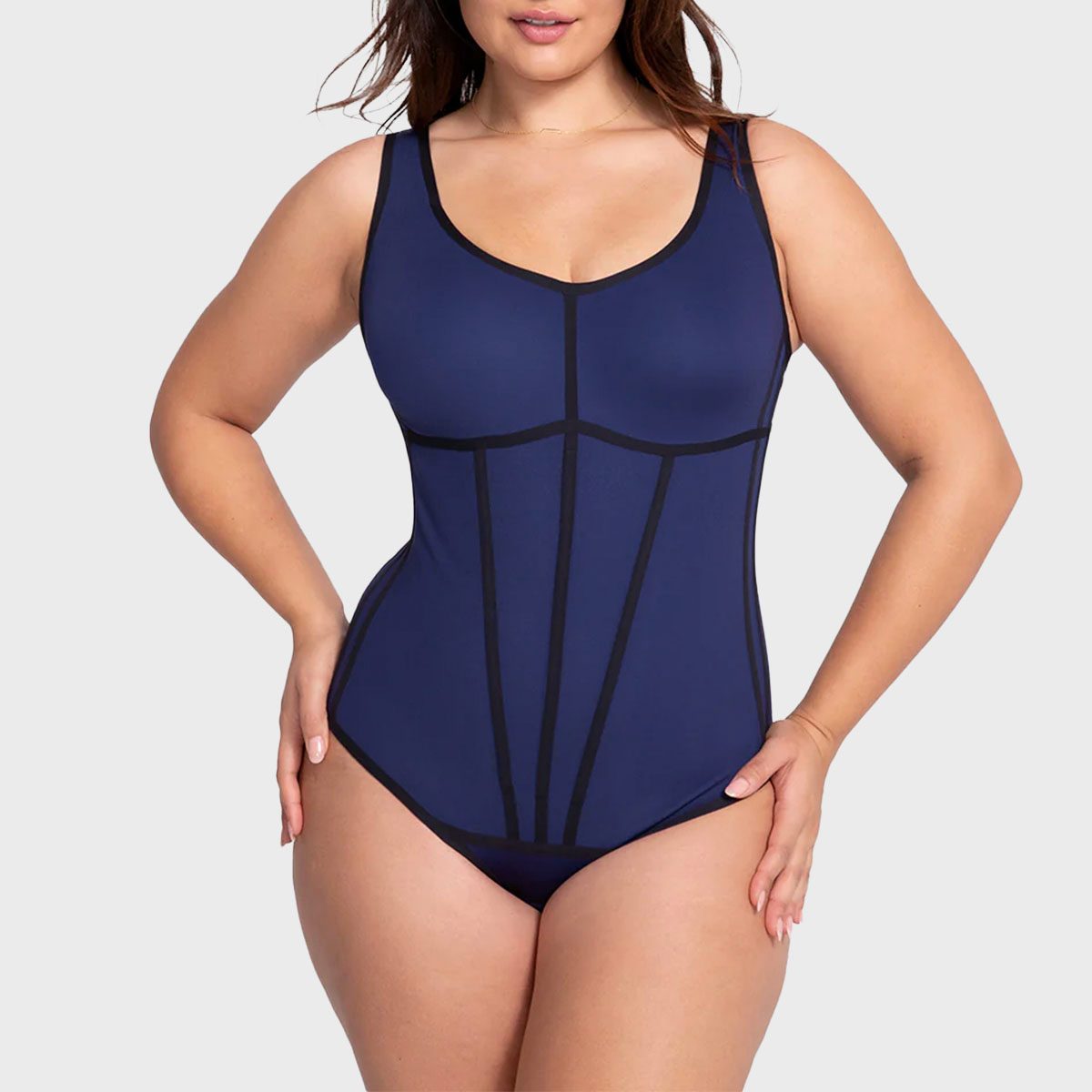 A person wears a form-fitting, navy blue one-piece swimsuit with black lines, standing against a plain light background.