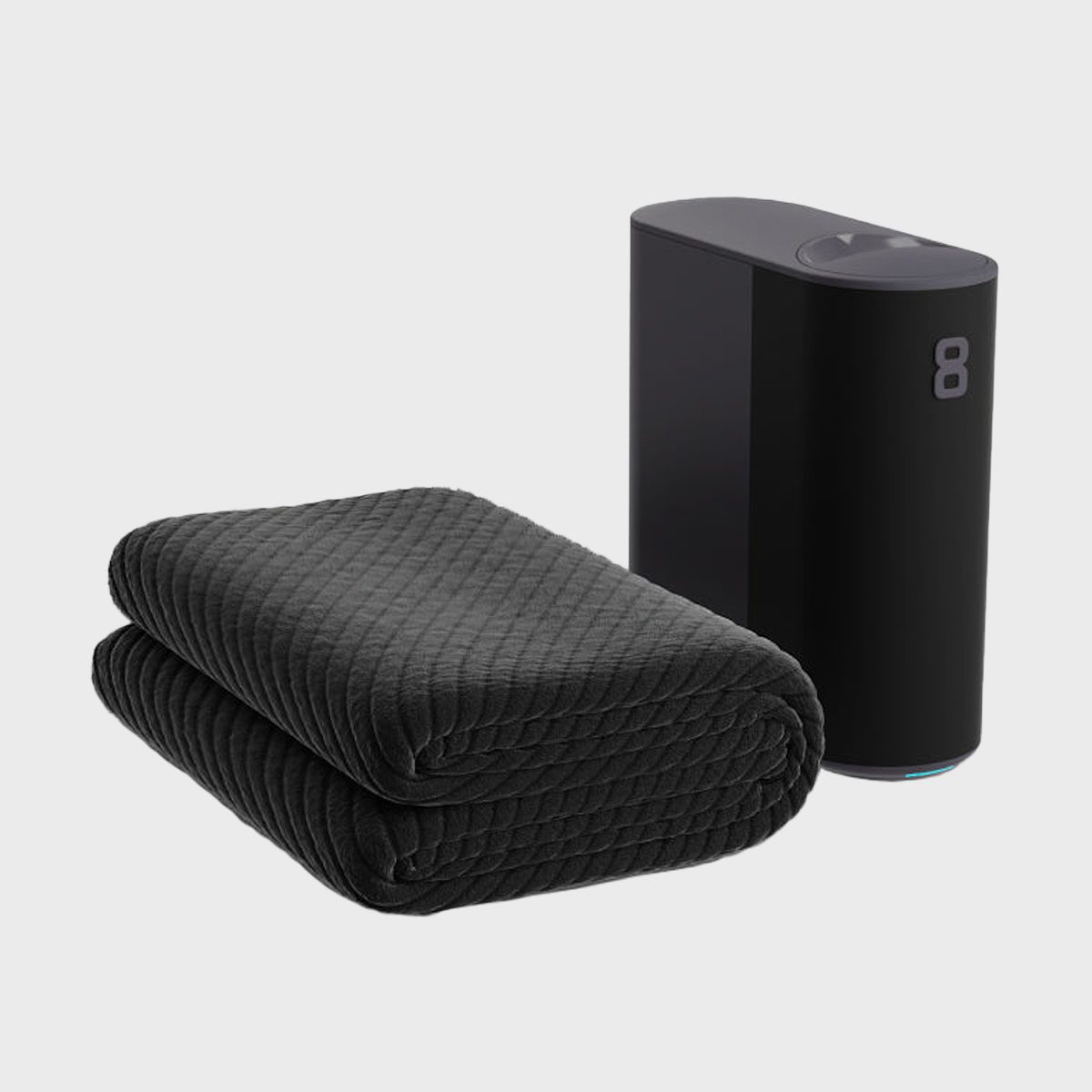 A folded, textured black blanket rests beside a sleek, black device with the number "8" in a minimalist setting.