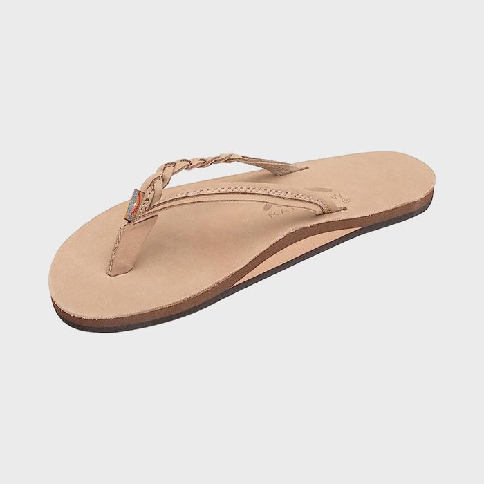 Beige flip-flop sits on a white background, featuring a braided strap and small rainbow tag.