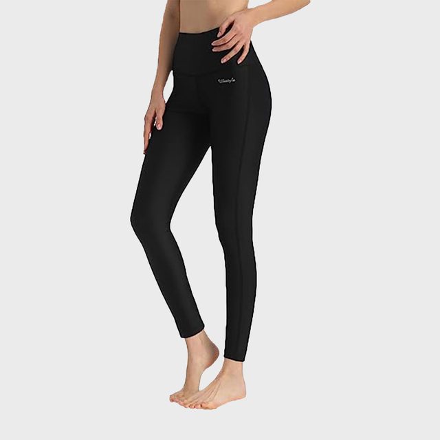 Woman wearing black leggings standing, with hands on her waist, on a plain white background.
