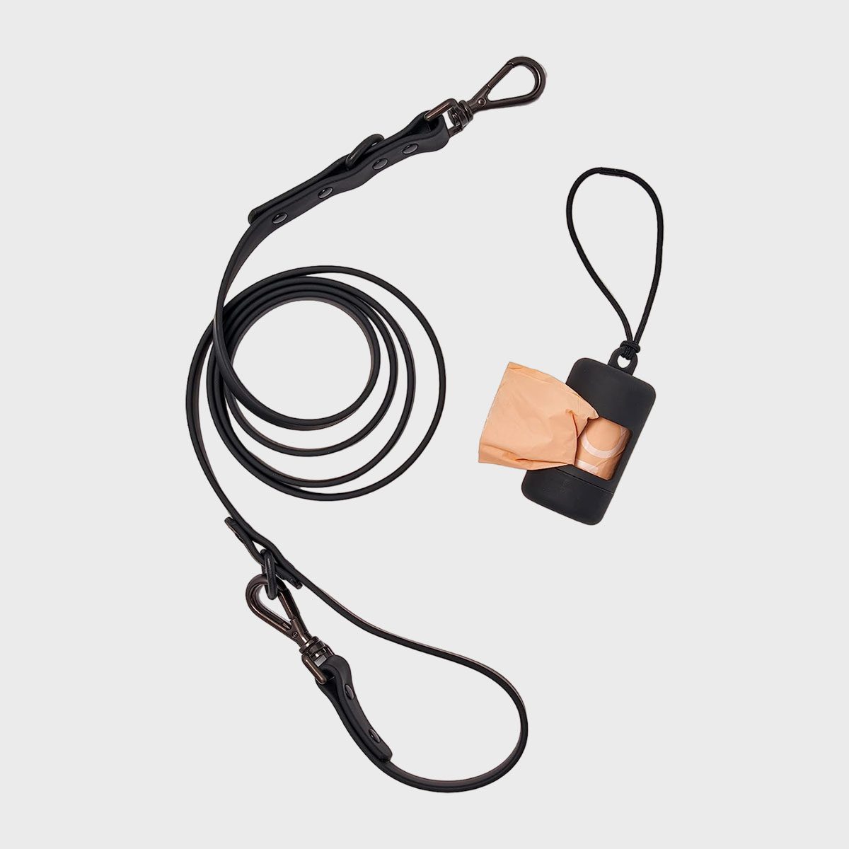 Black dog leash lies coiled beside a black dispenser containing orange waste bags on a light gray background.